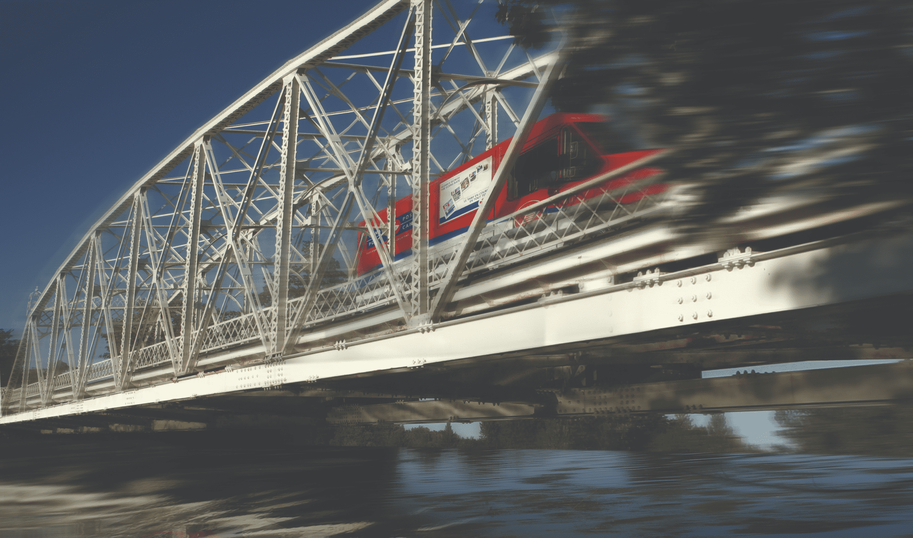 A red Canada Post truck drives over a steel bridge. 