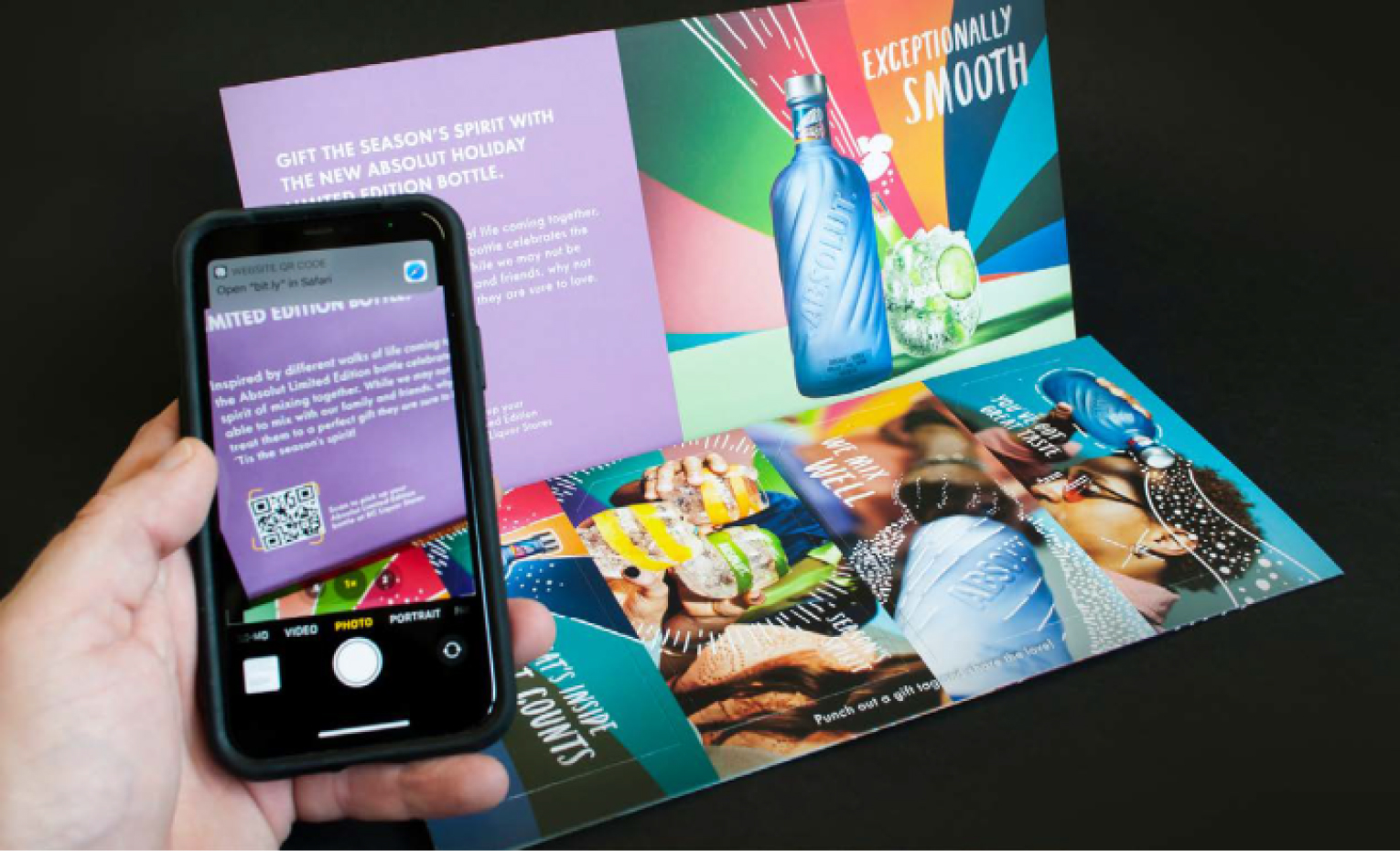 A person takes a cell phone photo of a QR code that appears on an Absolut Vodka direct mail piece.