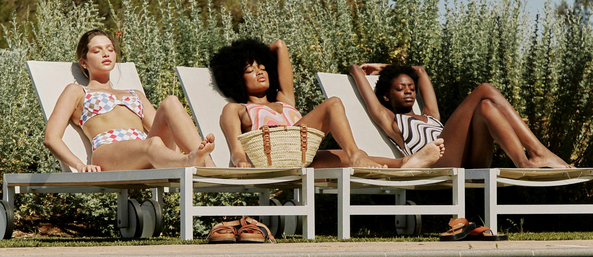 Three women sunbathe by a pool. 