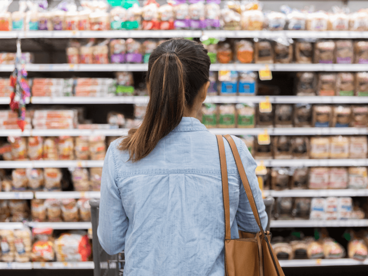 A woman stands in a supermarket isle, looking at the stocked shelves. 