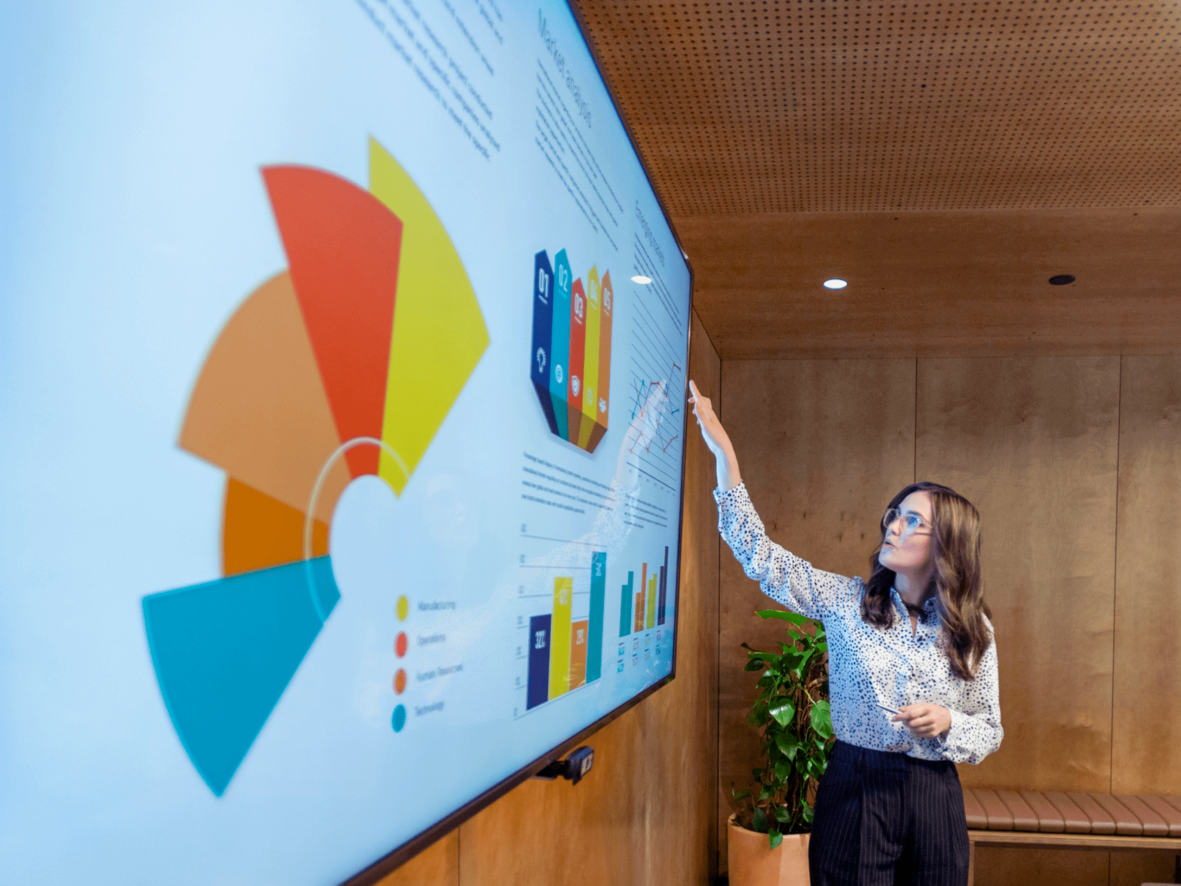 A woman presents data visualization charts and graphs on a large touch screen in a boardroom. 
