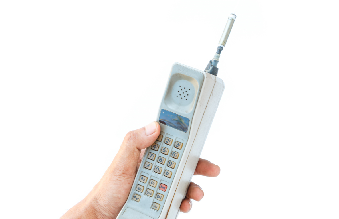 A person holds a large, first-generation cell phone with a long antenna.