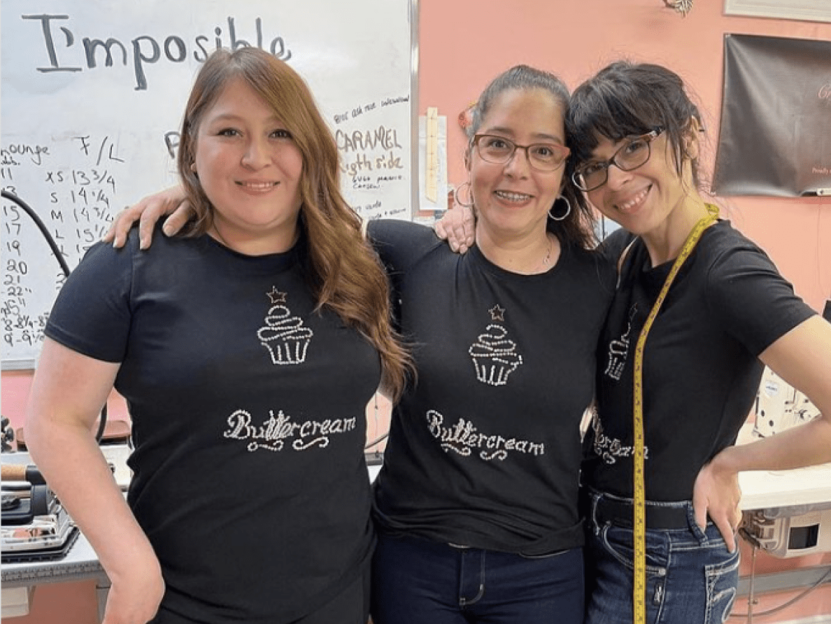 Three women embrace and wear the same black t-shirt that reads "Buttercream."