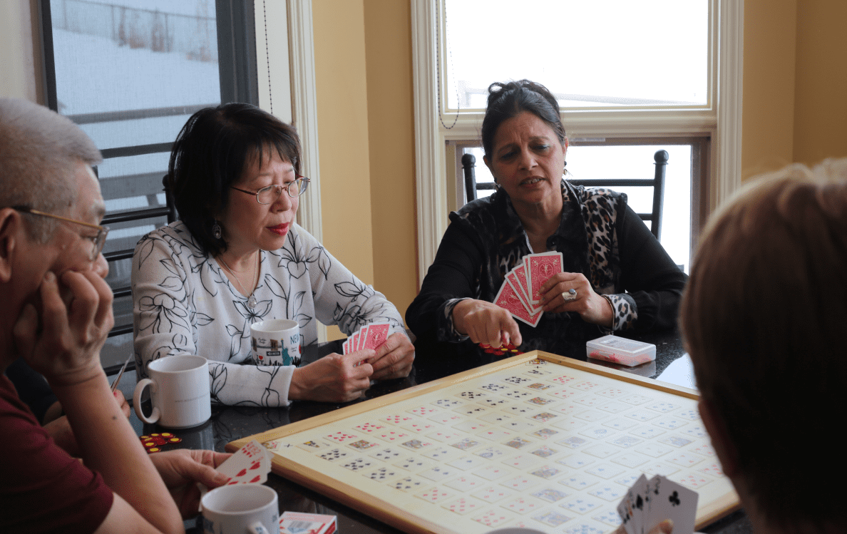 A group of senior citizens play a game of cards at a round table.