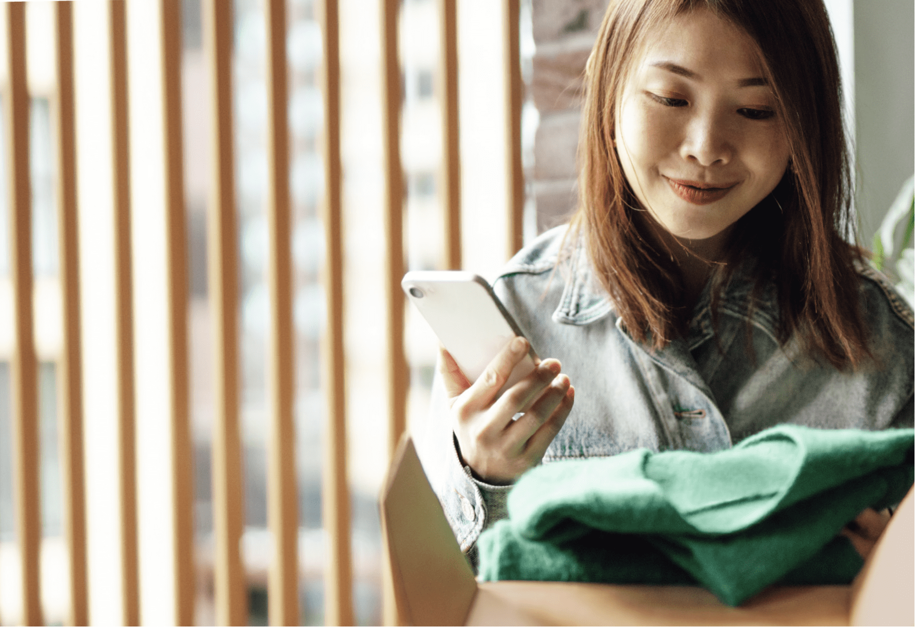 A smiling woman looks at a shipping package while holding her smart phone.