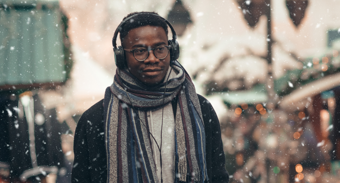 A man wearing a scarf and headphones walks outdoors as light snow falls.