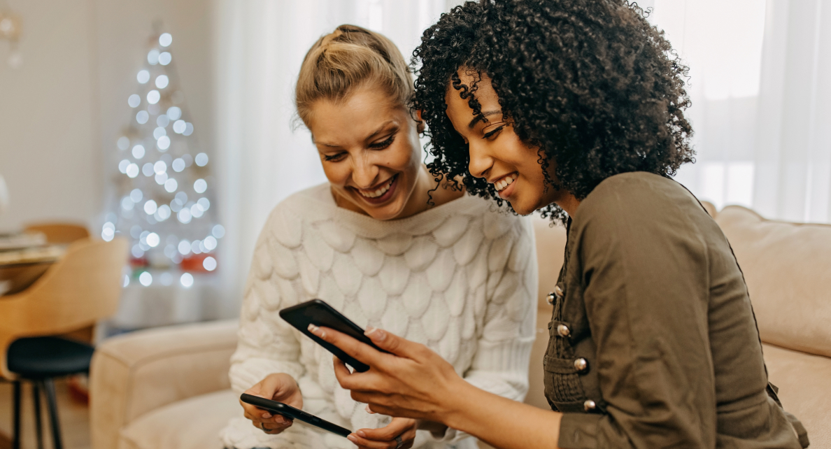 Two smiling women look at the same smartphone screen. 