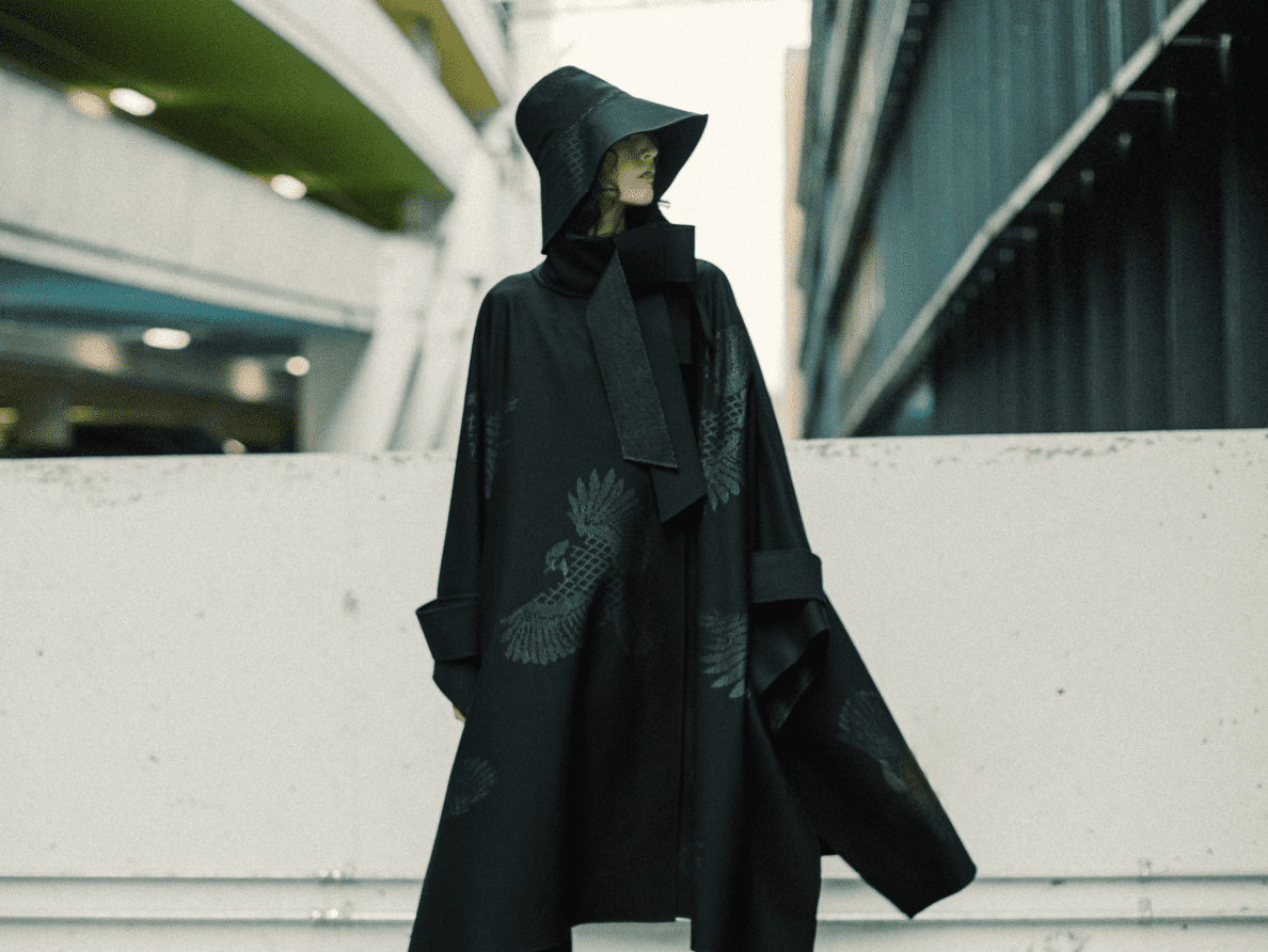 ALT EN A model wears a long black cape from Cape de Cœur and a matching black bucket hat. 