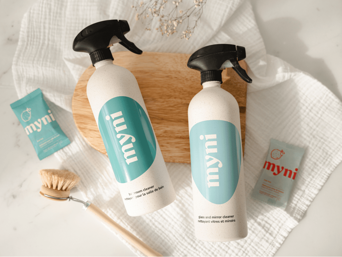 Four myni household products rest on table beside a scrub brush.