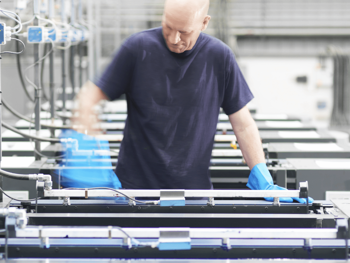 A man in a blue t-shirt and rubber gloves works in a print shop. 