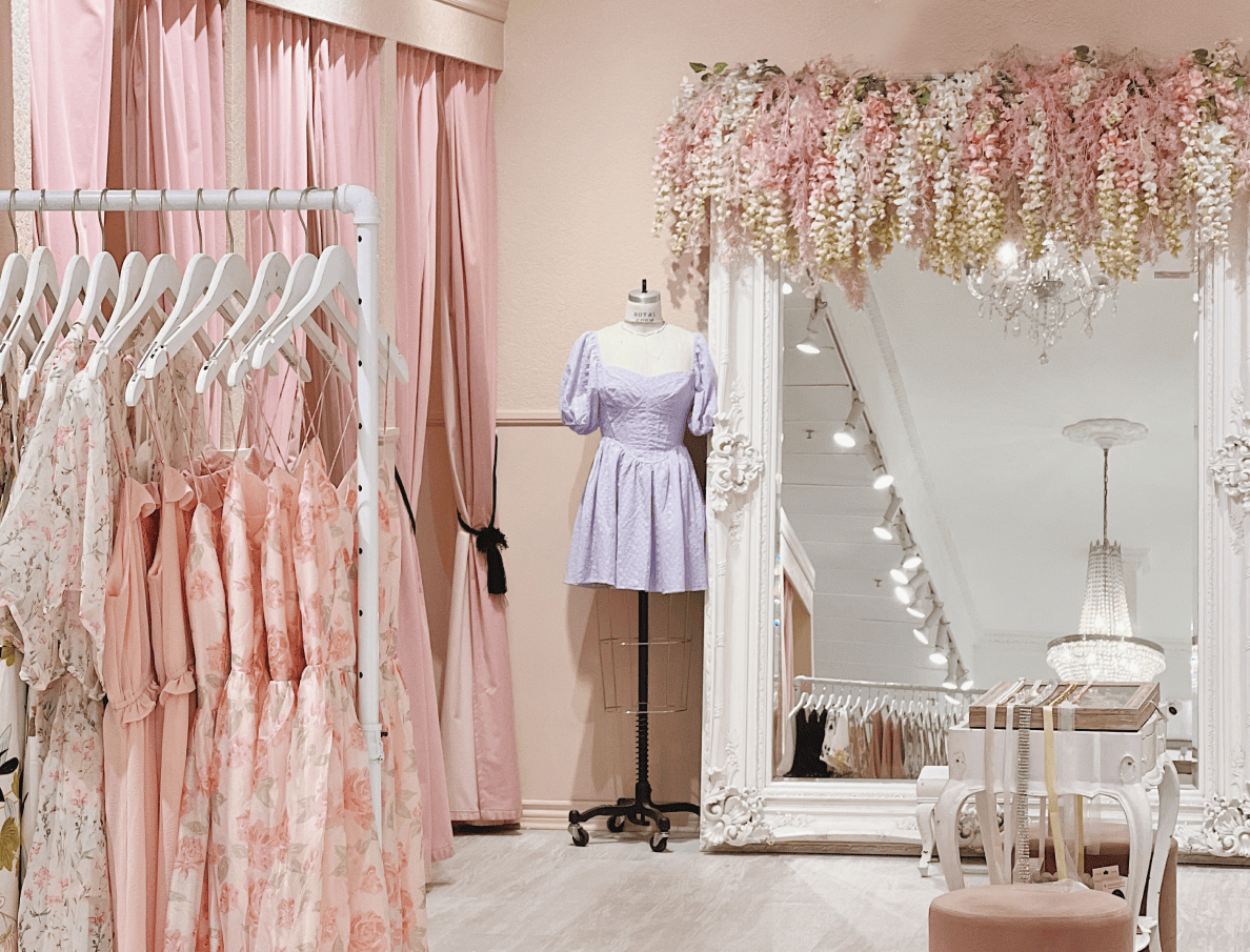 The changeroom at Boutique 1861 features a large mirror, pink curtain changing stalls and a rack of dresses.