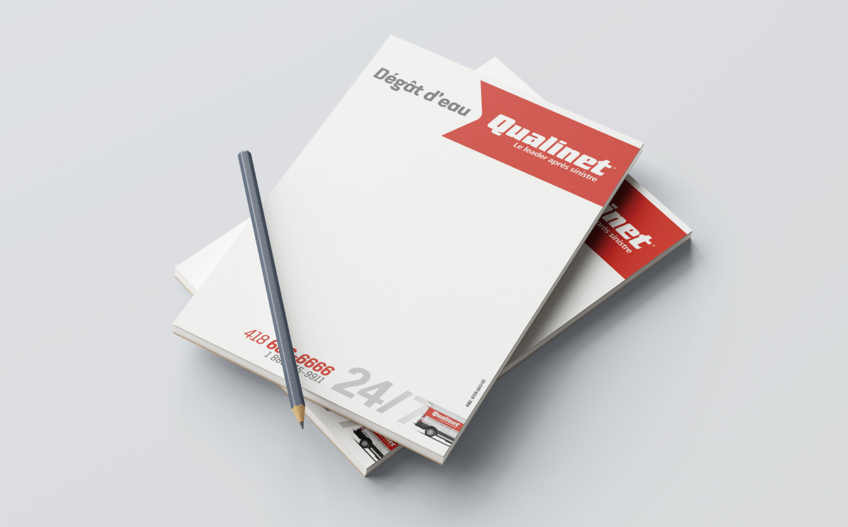 Stack of Qualinet notepads labeled “Dégât d’eau,” (water damage) with emergency contact numbers and a pencil placed on top.