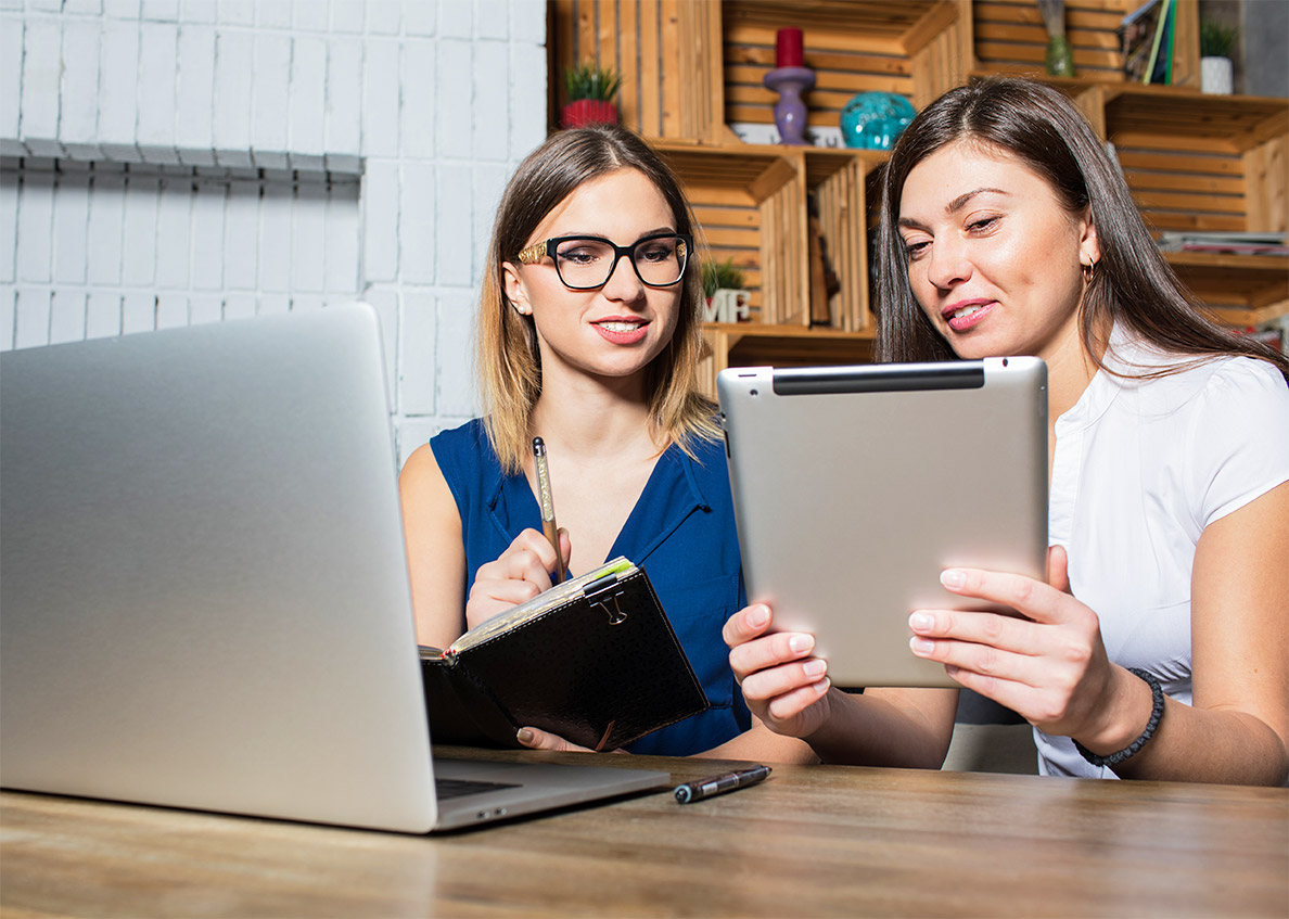 Two retail merchants review their e-commerce orders on a tablet and laptop.