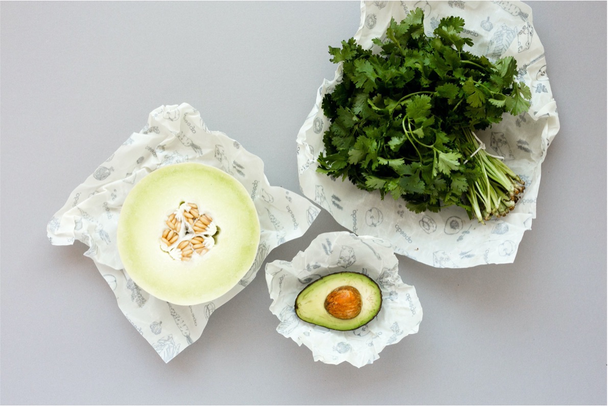 La moitié d’un melon miel et la moitié d’un avocat reposent sur des emballages Abeego. Un bouquet de persil repose sur un emballage Abeego.