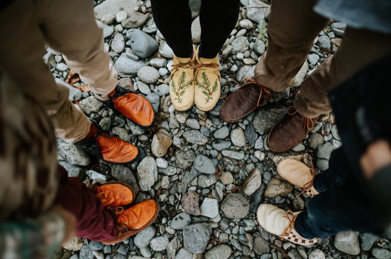 Cinq personnes se tiennent debout en cercle et portent des mocassins faits à la main de la marque Jamie Gentry Designs.