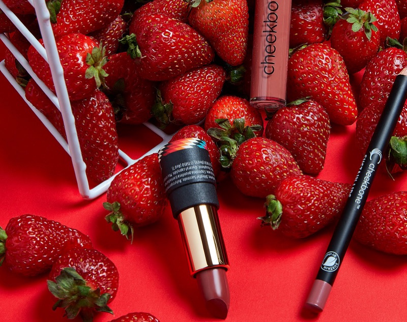Rouge à lèvres, colorant à lèvres et crayon contour des lèvres de la marque Cheekbone Beauty entourés de fraises