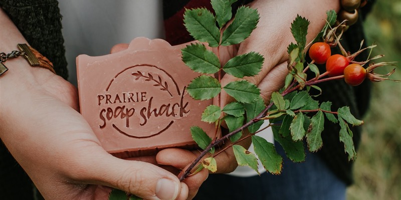 A woman holds a bar of Prairie Soap Shack brand soap and native prairie plant. 
