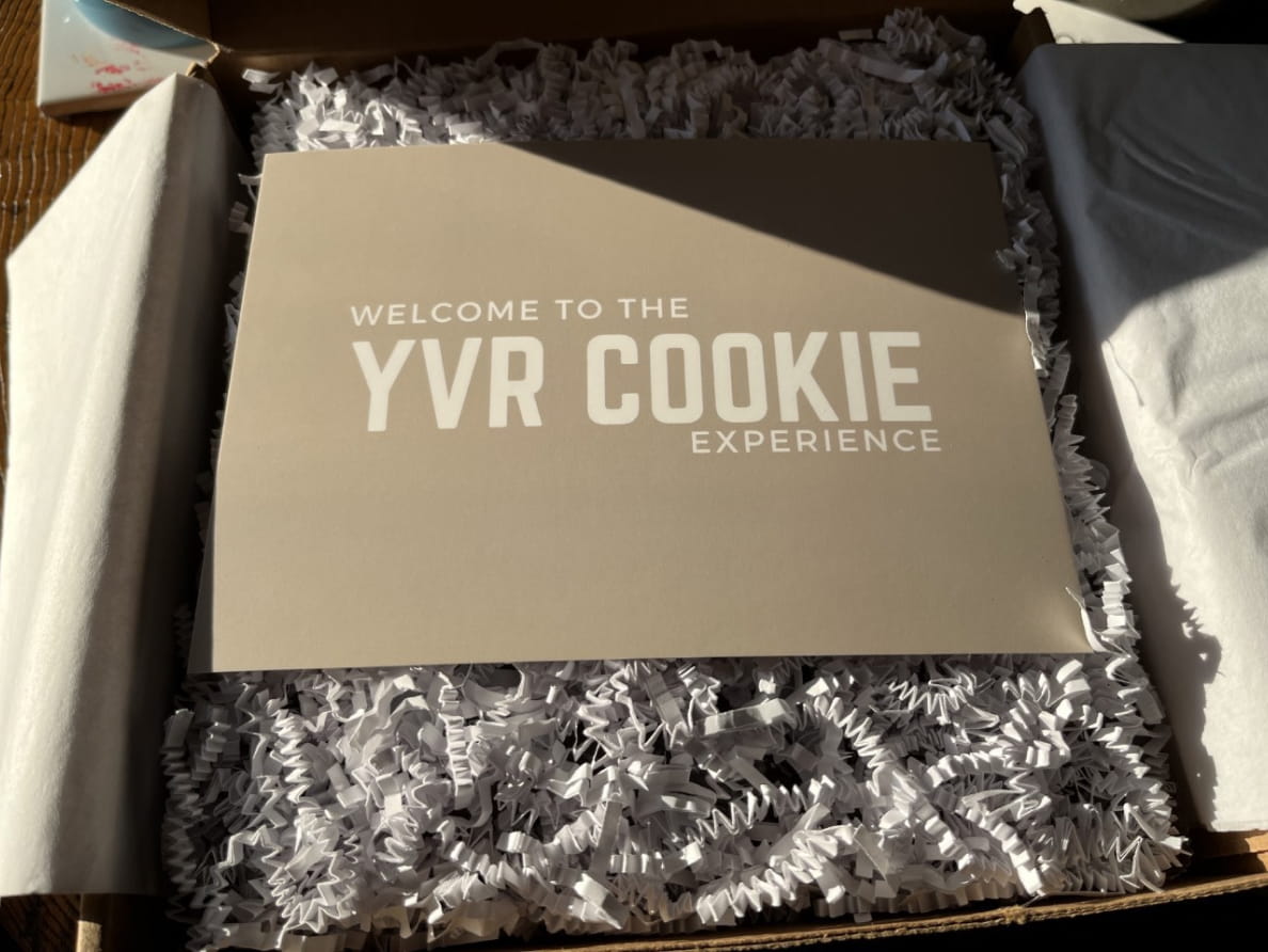 Boîte de biscuits YVR ouverte avec carton souhaitant « Welcome to the YVR COOKIE experience »
