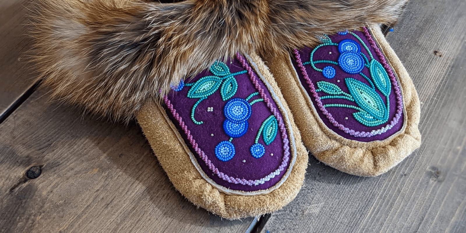 A pair of fur-lined moccasins adorned with green, blue and purple beads in a floral pattern. 