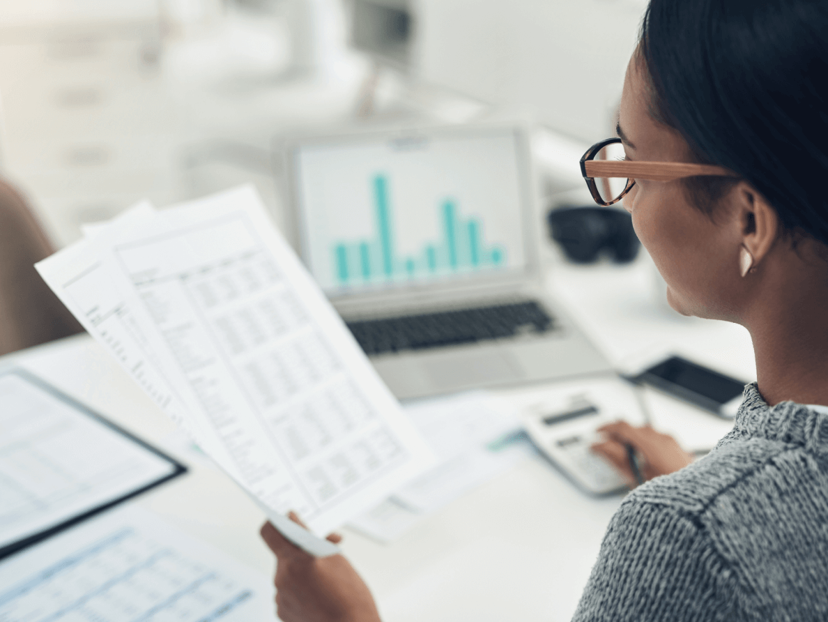 Assise à son bureau, une femme additionne des chiffres à l’aide de sa calculette.