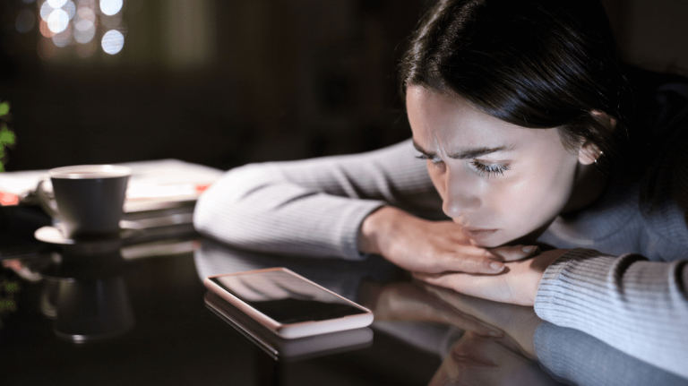 Une jeune femme regarde pensivement l’écran éteint de son téléphone intelligent.