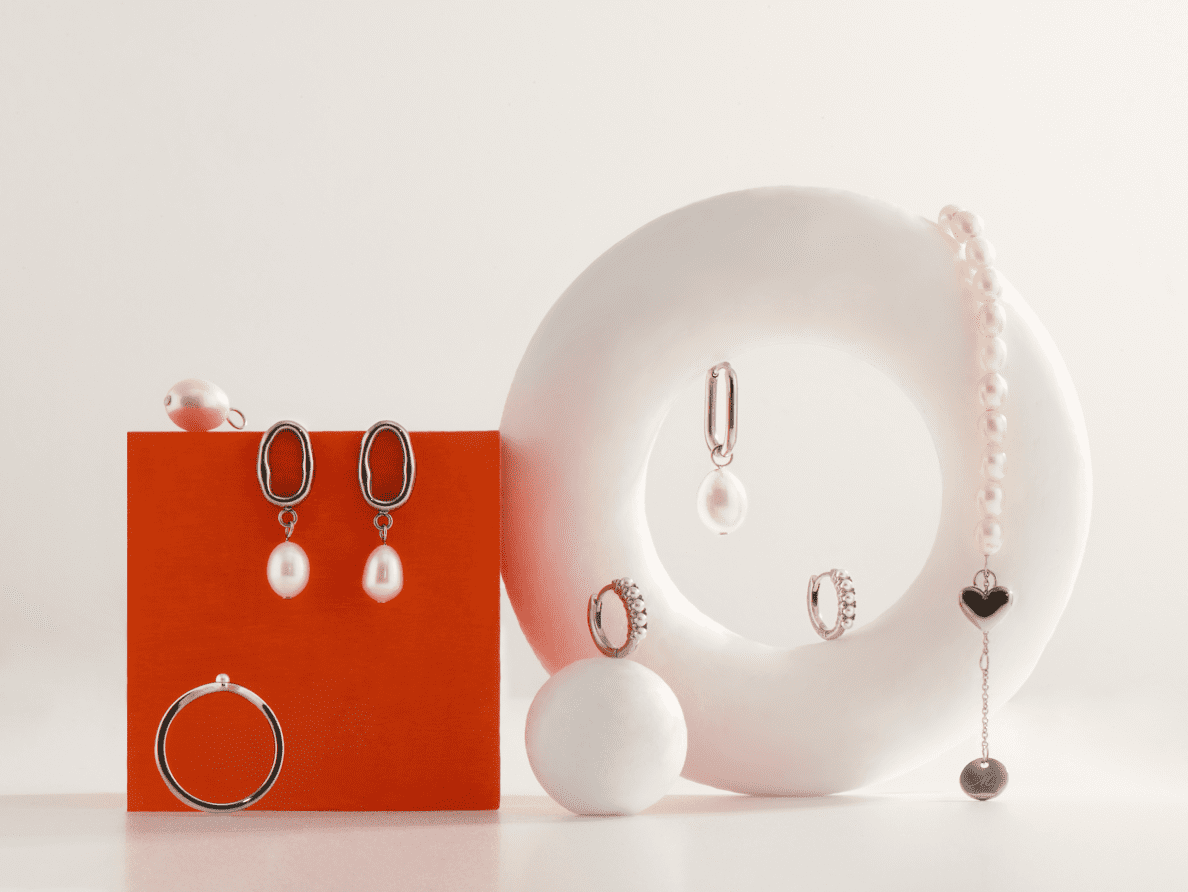 Dormeuses avec perle, bagues et bracelet de perles de Mia Bijoux, disposés sur un bloc rouge, une sphère blanche et un anneau blanc
