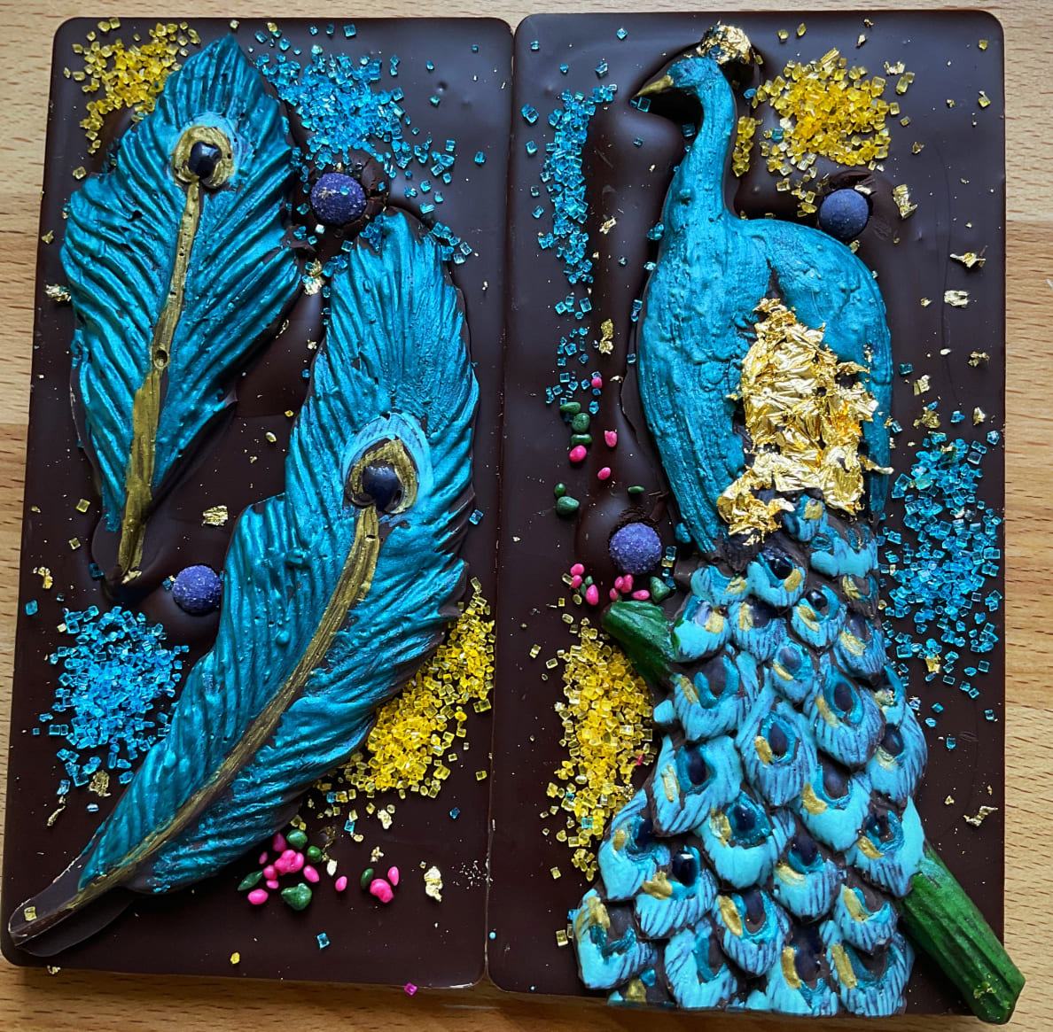 Deux tablettes de chocolat de Raven Rising Global-Indigenous Chocolates; l’une est ornée d’un paon bleu et doré et l’autre, de plumes de paon assorties