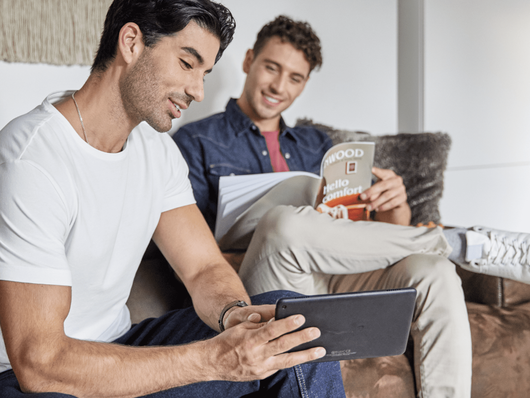 Assis un à côté de l’autre sur un sofa, un homme montre l’écran de sa tablette au second.