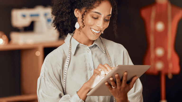 Une femme portant un ruban à mesurer au cou consulte une tablette intelligente dans son atelier de couture.