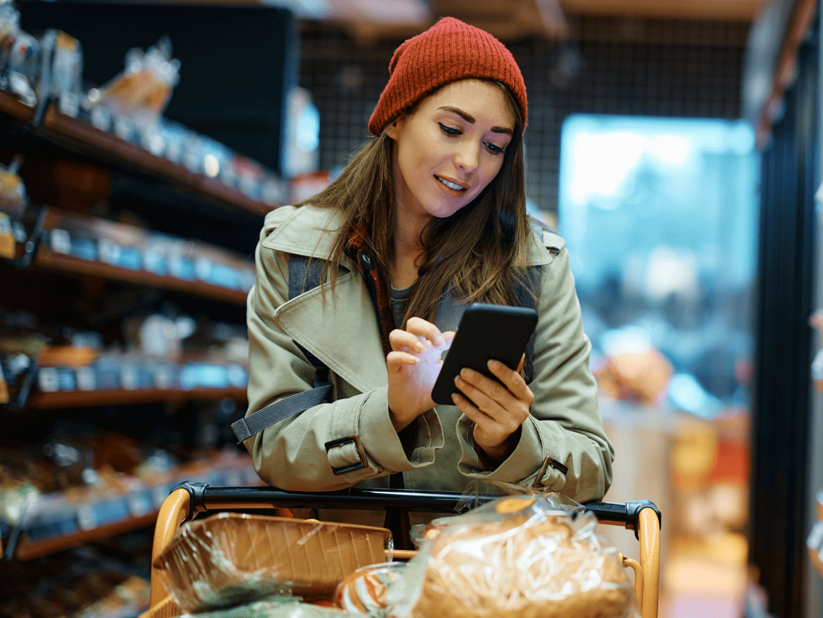 Dans une épicerie, une jeune femme au béret rouge utilise son téléphone intelligent.