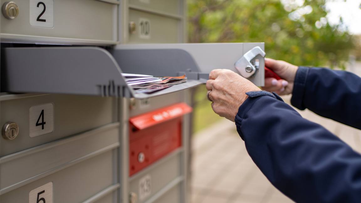 Close up of hands opening a community mailbox and sliding out an accessible compartment tray containing mail. Close up of hands opening a community mailbox and sliding out an accessible compartment tray containing mail.