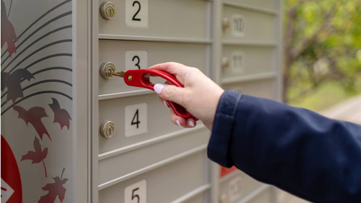 Close up of a hand using an accessible key turner to unlock a community mailbox compartment.