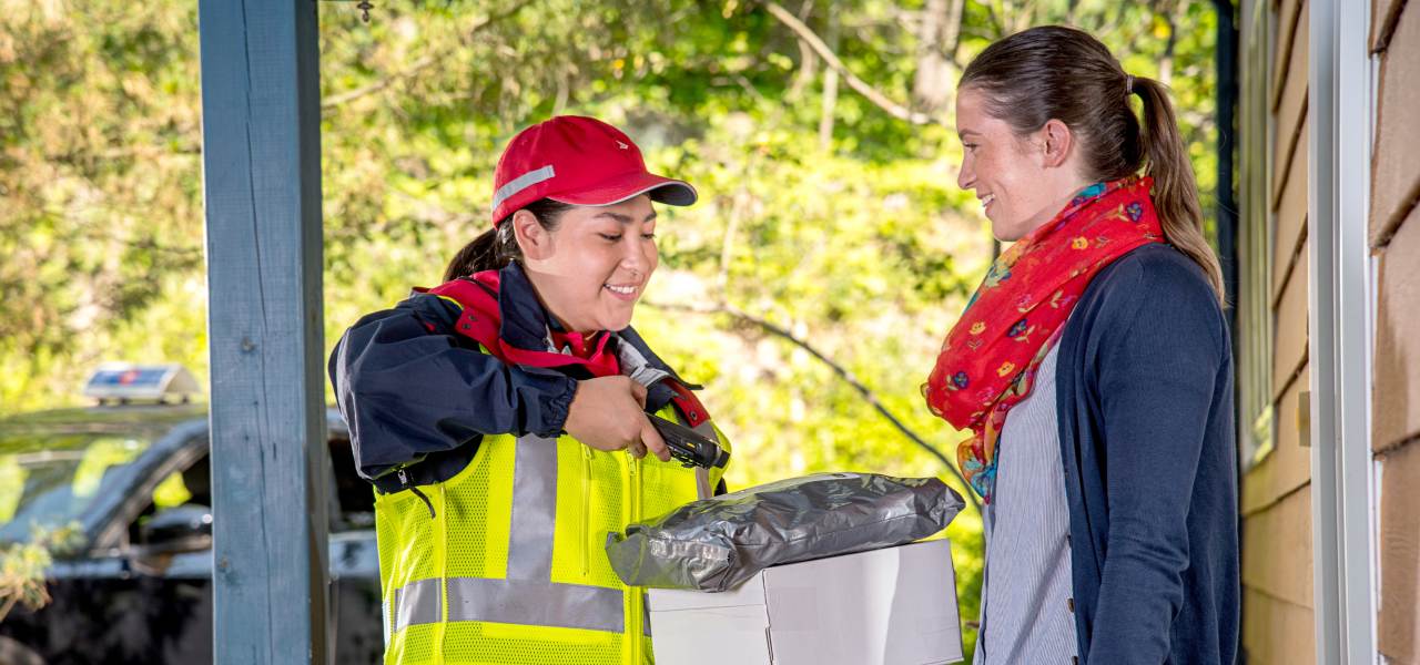 Example of a photo that can be used by accredited media. Features a Canada Post delivery agent delivering a package to a woman outside her home.