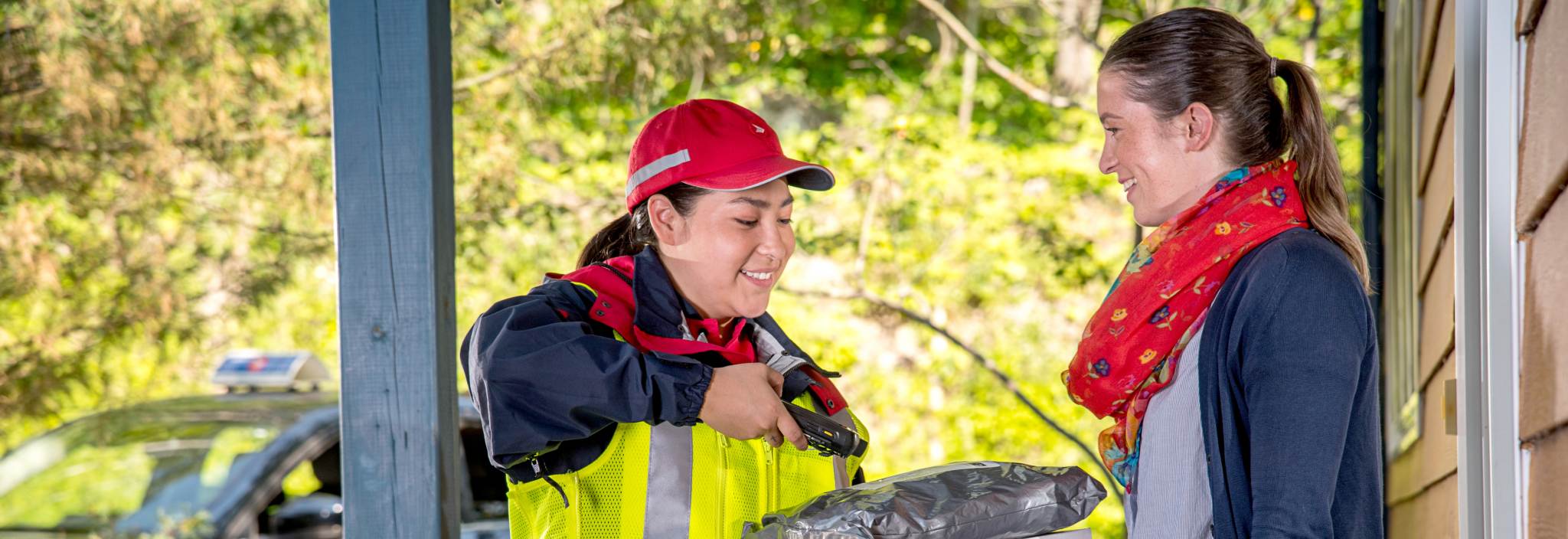 Example of a photo that can be used by accredited media. Features a Canada Post delivery agent delivering a package to a woman outside her home.