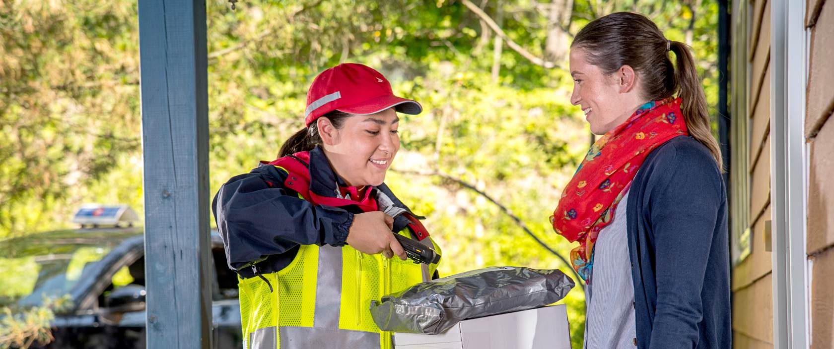 Example of a photo that can be used by accredited media. Features a Canada Post delivery agent delivering a package to a woman outside her home.