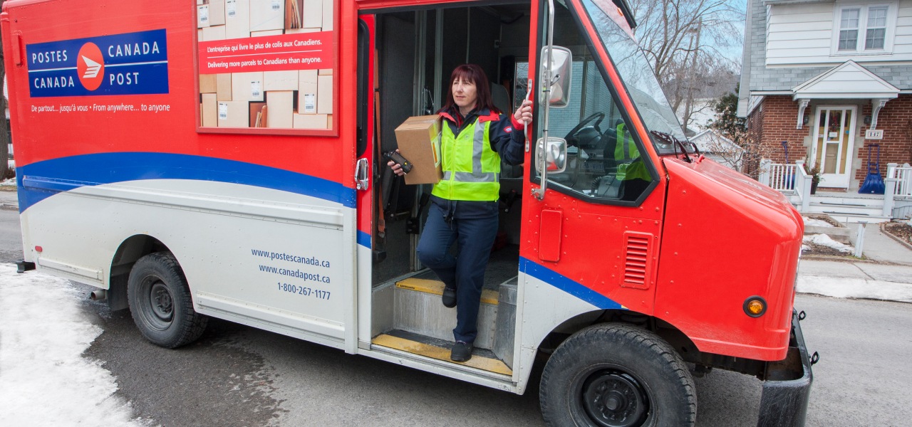 Delivery agent stepping out of a Canada Post truck in a residential neighbourhood to deliver a package