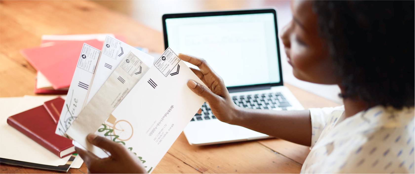 A woman at her desk holds a small stack of business mail. A Canada Post postal indicia is printed on the upper right-hand corner of each envelope.