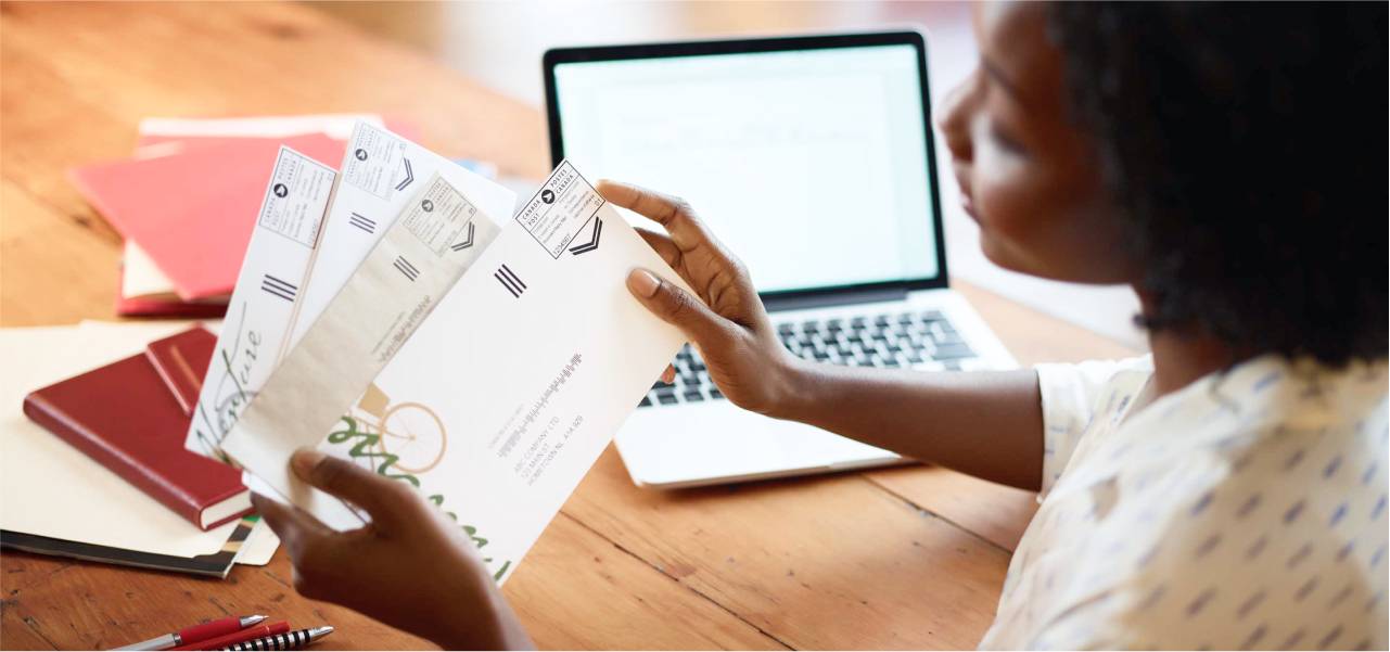 A woman at her desk holds a small stack of business mail. A Canada Post postal indicia is printed on the upper right-hand corner of each envelope.