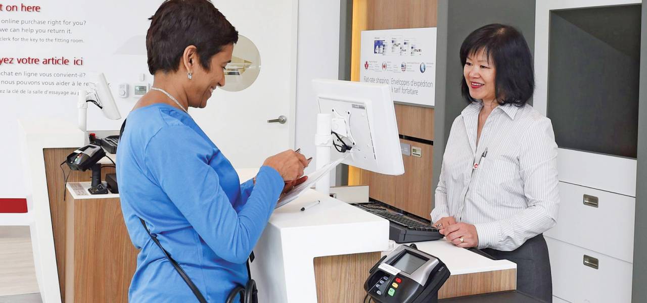 A woman completes her ID verification process at a Canada Post counter by presenting her government-issued photo ID.