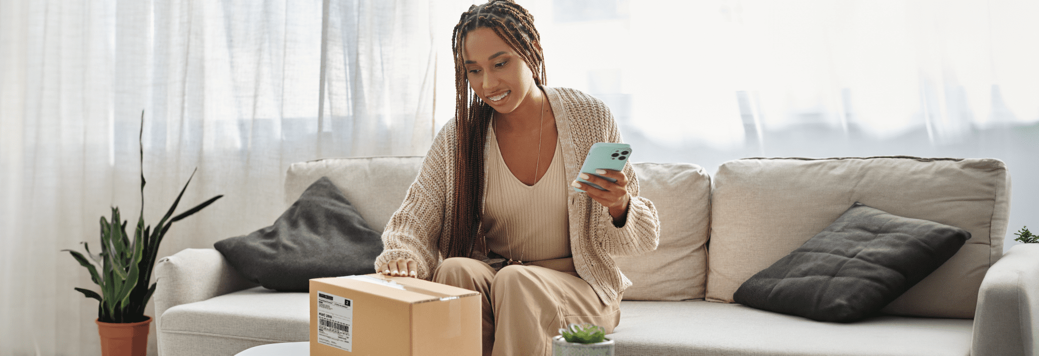 A smiling woman looks at her smart phone as she holds a package
