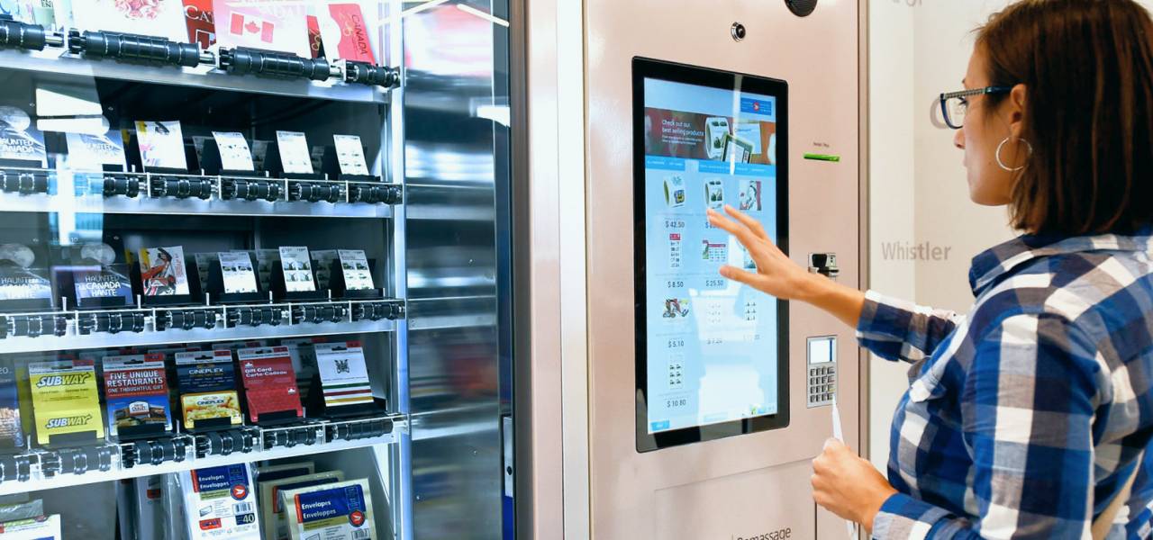 A woman uses a touchscreen to purchase a gift card from a Canada Post self-serve vending machine.