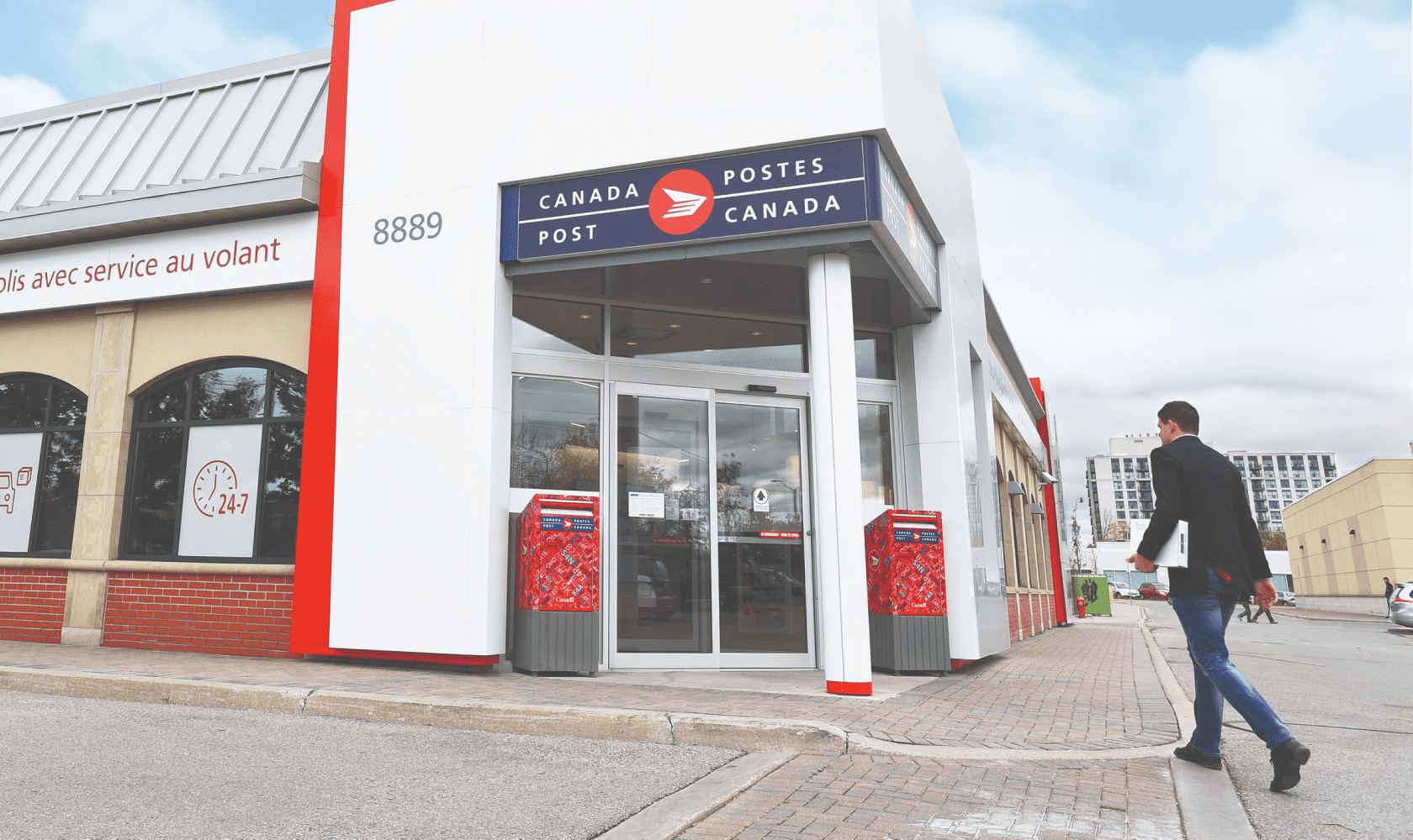 A man walks into a Canada Post retail location with a package under his arm.