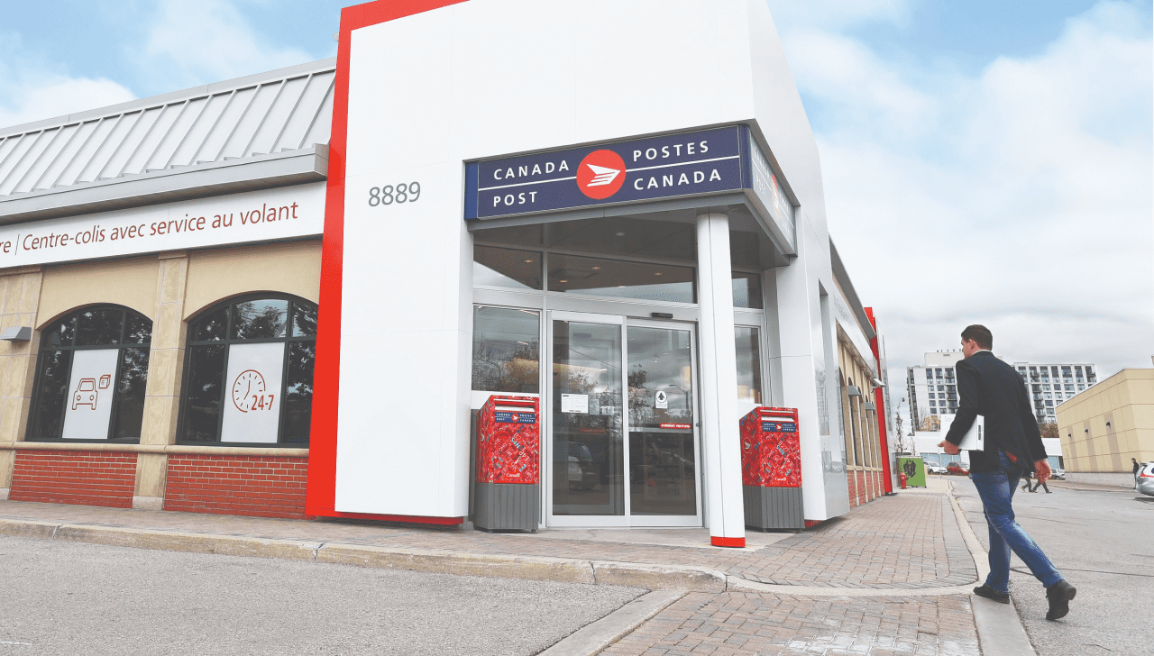 A man walks into a Canada Post retail location with a package under his arm.