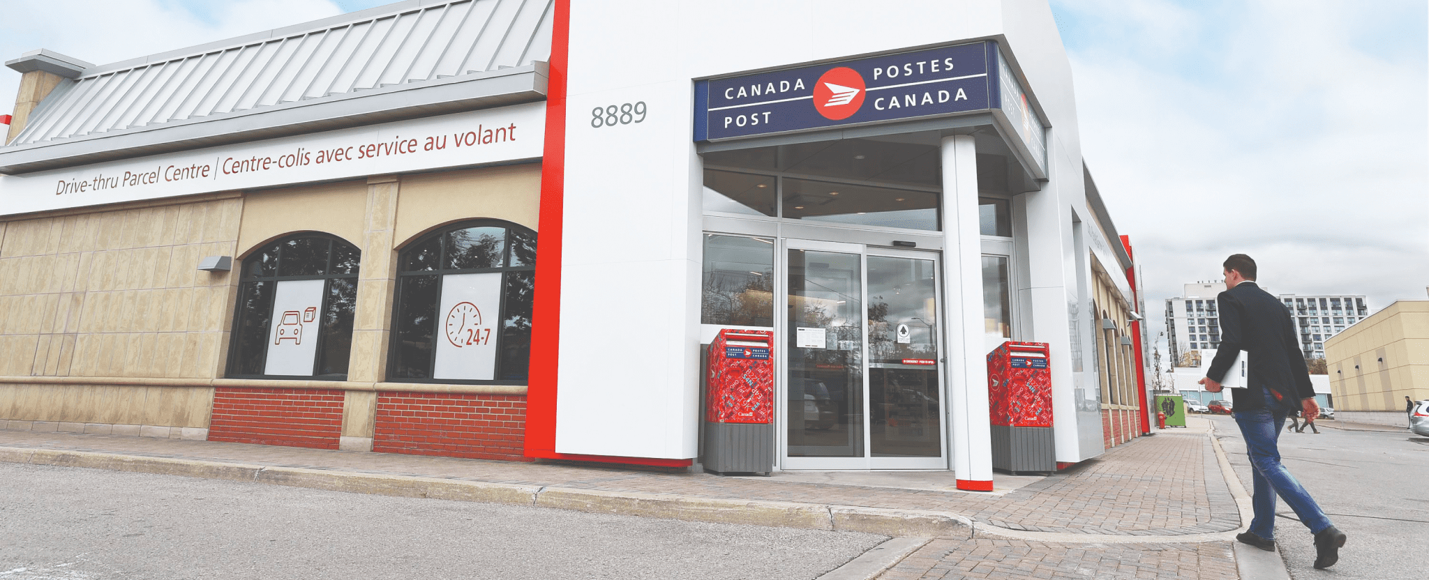 A man walks into a Canada Post retail location with a package under his arm.