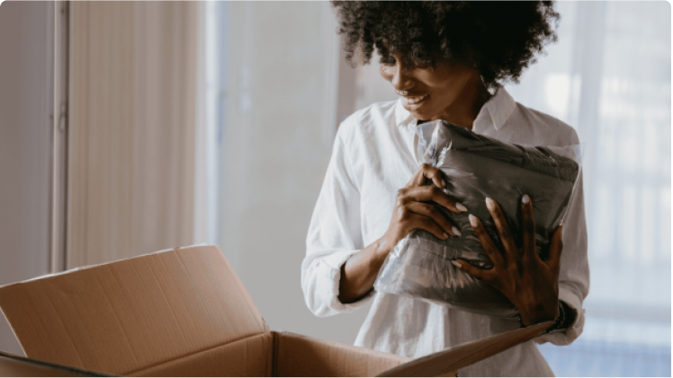 A woman smiles and holds a wrapped item as she looks down into an open shipping box.