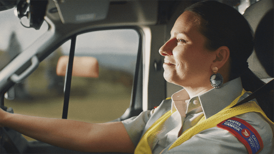 Une employée de Postes Canada sourit en conduisant un camion.