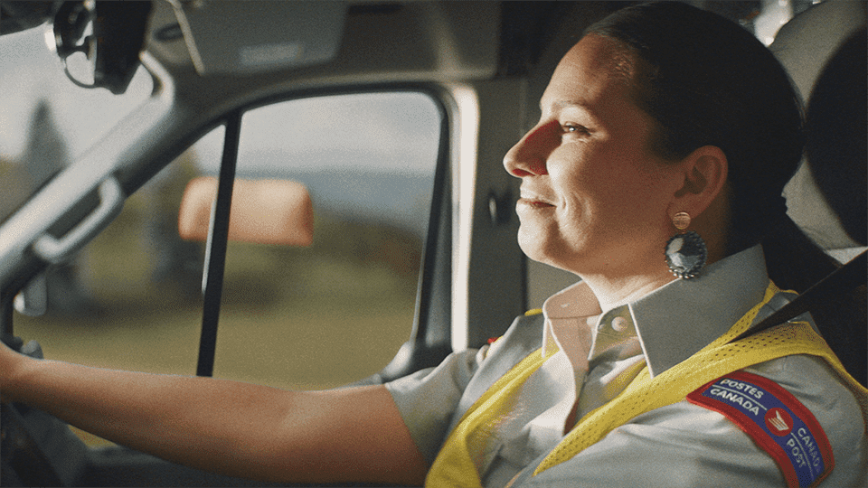 A Canada Post employee smiles as she drives a truck.