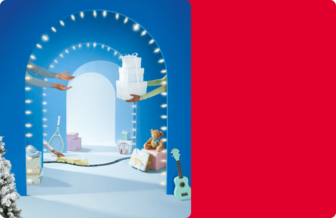 A blue hallway is lined with holiday gifts. A woman hands a man a stack of wrapped gifts.