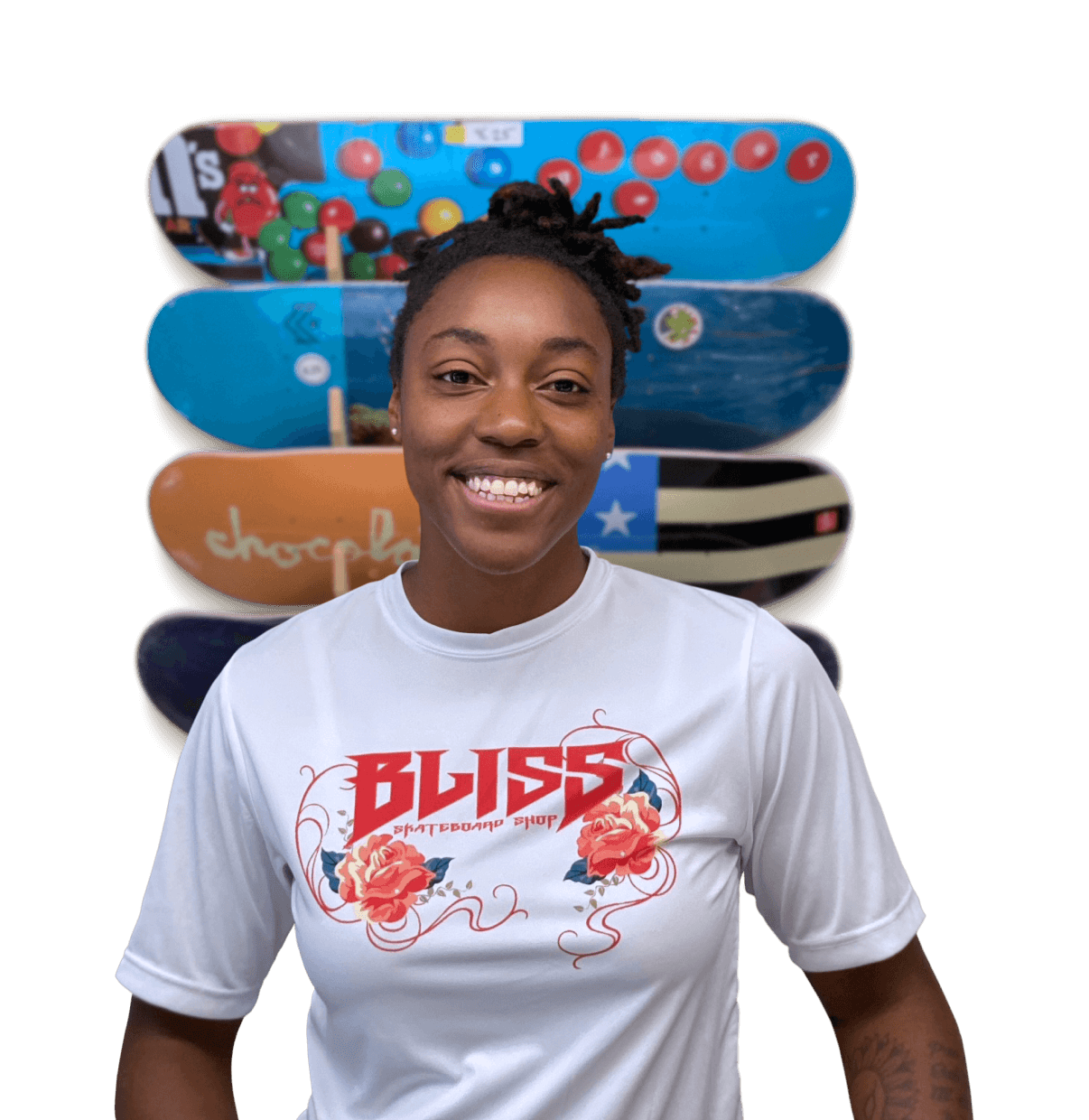 Sasha Senior, Founder of Bliss Skateboard Shop, stands and smiles in front on colourful skateboards mounted on a wall.