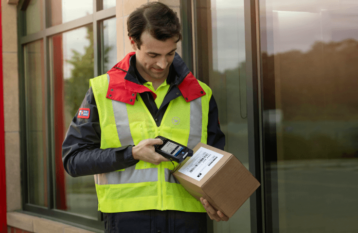 A Canada Post employee wearing a yellow safety vest scans a package while out for delivery.